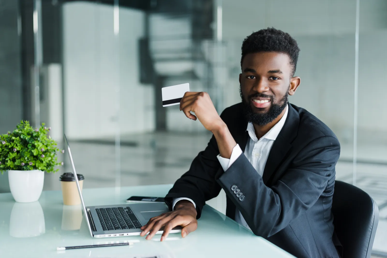A man holding a bank card while working on a laptop in an office